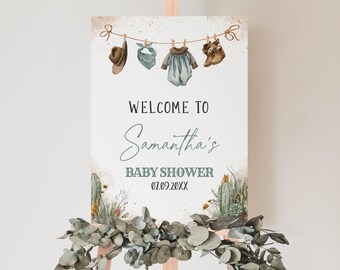 May include: A baby shower welcome sign on an easel. The sign features a watercolor design with a cowboy hat, bandana, baby clothes, and boots hanging on a clothesline. The text reads "Welcome to Samantha's Baby Shower 07.09.20XX."