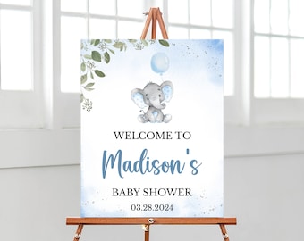 May include: A baby shower welcome sign with a watercolour illustration of a grey elephant holding a blue balloon. The sign reads "Welcome to Madison's Baby Shower 03.28.2024" with blue and black text on a white background with blue watercolour accents.