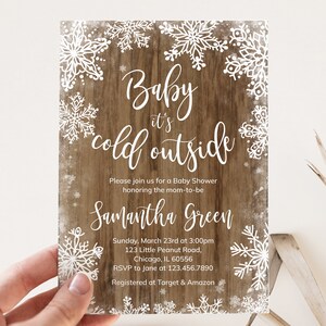 Puede incluir: Invitación a un baby shower con un fondo de madera rústica y un borde de copos de nieve blancos. El texto dice "Baby it's cold outside" con detalles del evento, incluido el nombre de la futura madre, la fecha, la hora y el lugar.