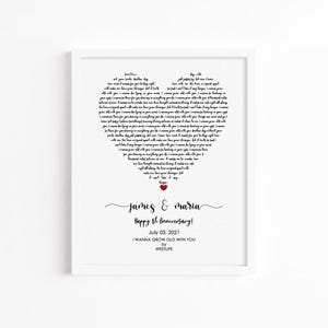 May include: A framed print with a heart-shaped design composed of song lyrics. The names "James & Maria" and "Happy 1st Anniversary!" are written below the heart. A small red heart is at the bottom of the heart-shaped lyrics.