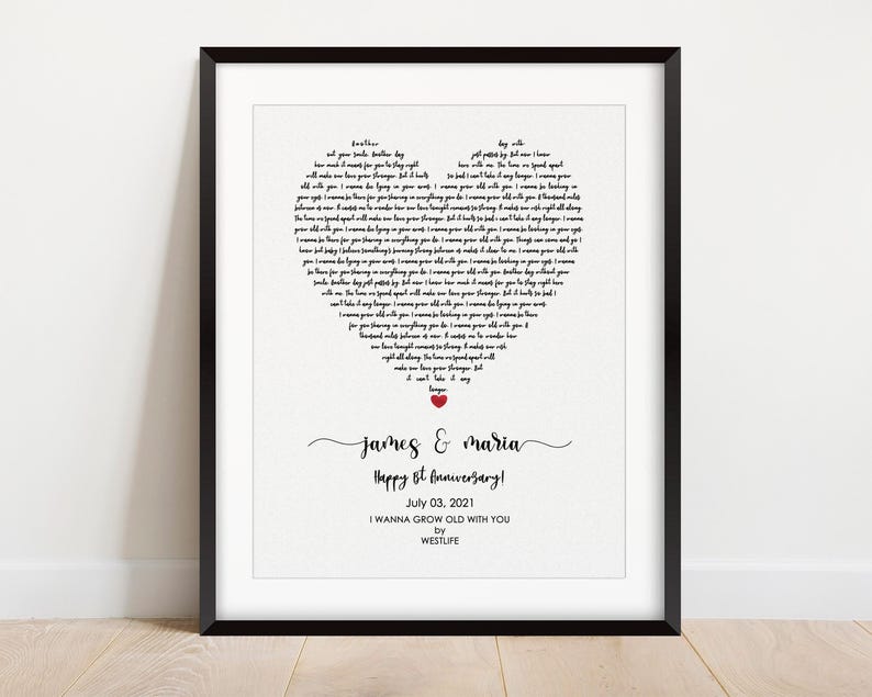 May include: A framed print with a black border. The print features lyrics arranged in a heart shape. Below the heart, the names "James & Maria" are written in cursive, followed by "Happy 1st Anniversary!" and the date "July 03, 2021". The song title "I WANNA GROW OLD WITH YOU" is also included.