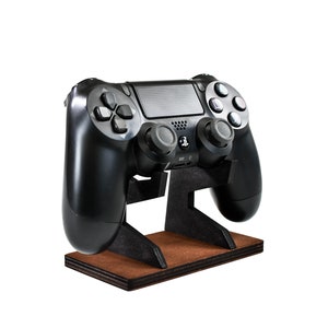 May include: A black PlayStation 4 controller sits on a wooden stand. The controller is in a vertical position with the buttons facing forward.