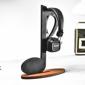 May include: Black wooden headphone stand shaped like a musical note. The stand has a brown base and is holding a pair of black headphones.