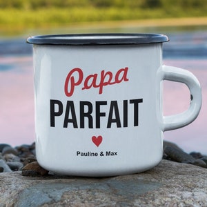 Pu&ograve; includere: Tazza in smalto bianco con bordo e manico neri. La tazza ha testo nero che recita "Papa Parfait" con un cuore rosso e il testo "Pauline & Max". La tazza &egrave; appoggiata su una roccia vicino a un fiume.