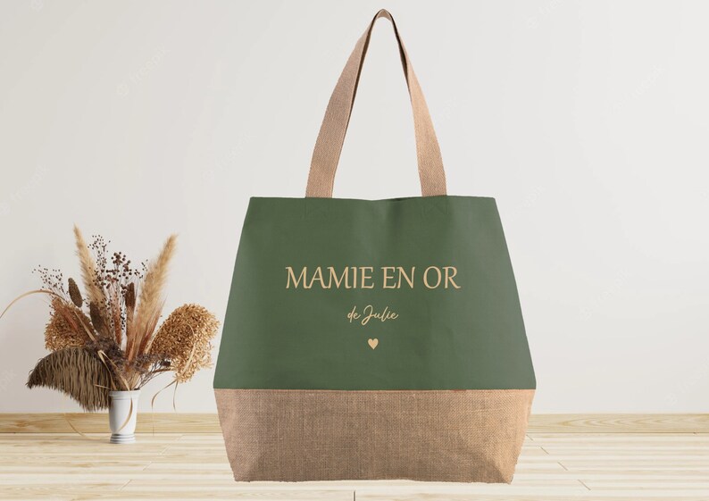 K&ouml;nnte beinhalten: Eine gr&uuml;ne und braune Einkaufstasche mit dem Text "MAMIE EN OR de Julie" und einem kleinen Herz.
