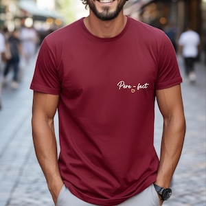 May include: Burgundy crew neck t-shirt with the text "P&egrave;re-fect" in white script and a small gold heart. The shirt is made of a soft material and has short sleeves.