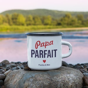 Pu&ograve; includere: Tazza in smalto bianco con bordo e manico neri. La tazza ha testo rosso e blu che dice "Papa Parfait" con un cuore rosso e il testo "Pauline & Max".