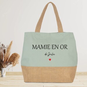 K&ouml;nnte beinhalten: Eine hellgr&uuml;ne Tragetasche mit dem Text "MAMIE EN OR de Julie" und zwei roten Herzen. Die Tasche ist aus Canvas und hat einen braunen Juteboden.