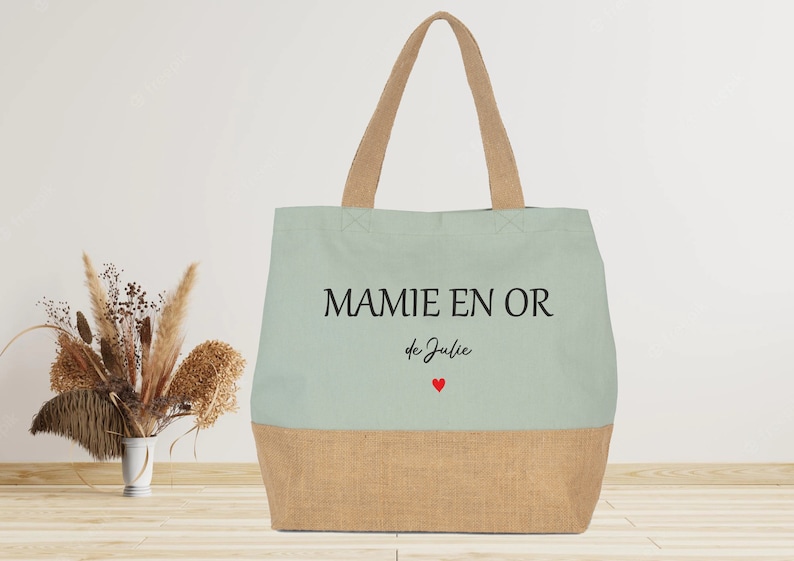 K&ouml;nnte beinhalten: Eine hellgr&uuml;ne Tragetasche mit dem Text "MAMIE EN OR de Julie" und zwei roten Herzen. Die Tasche ist aus Canvas und hat einen braunen Juteboden.