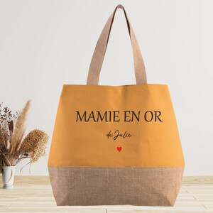 K&ouml;nnte beinhalten: Eine gelbe Tragetasche mit dem Text "MAMIE EN OR de Julie" und einem kleinen roten Herz. Die Tasche hat einen braunen Boden.