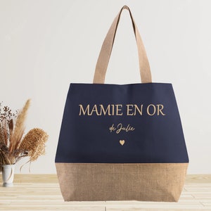 K&ouml;nnte beinhalten: Eine marineblaue Tragetasche mit braunem Juteboden. Die Tasche tr&auml;gt den Schriftzug "MAMIE EN OR de Julie" in goldenen Buchstaben mit einem kleinen goldenen Herz.
