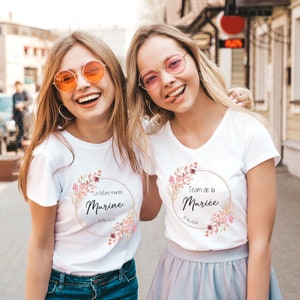 May include: Two women wearing white t-shirts with floral designs and text. One shirt says "La future mari&eacute;e Marine - 18 Mai 2024" and the other says "Team de la Mari&eacute;e - 18 Mai 2024". Both are smiling and wearing sunglasses.