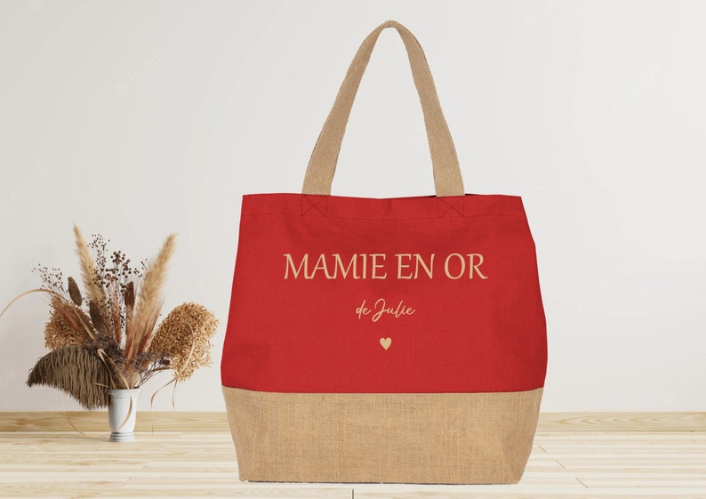 K&ouml;nnte beinhalten: Rote und braune Einkaufstasche mit dem Text "MAMIE EN OR de Julie" und einem kleinen Herz.