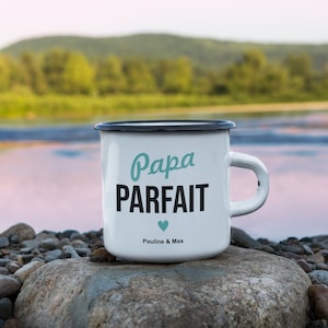 Pu&ograve; includere: Tazza in smalto bianco con bordo e manico neri. La tazza ha un design nero e turchese che dice "Papa Parfait" con un piccolo cuore turchese e il testo "Pauline & Max".