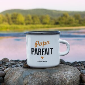 Pu&ograve; includere: Tazza in smalto bianco con bordo e manico neri. La tazza ha il testo "Papa Parfait" in nero con un piccolo cuore arancione e il testo "Pauline & Max" in nero pi&ugrave; piccolo.
