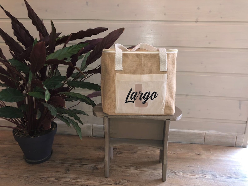 May include: A beige jute tote bag with a white fabric pocket on the front. The pocket has the word "Largo" printed in black cursive lettering.