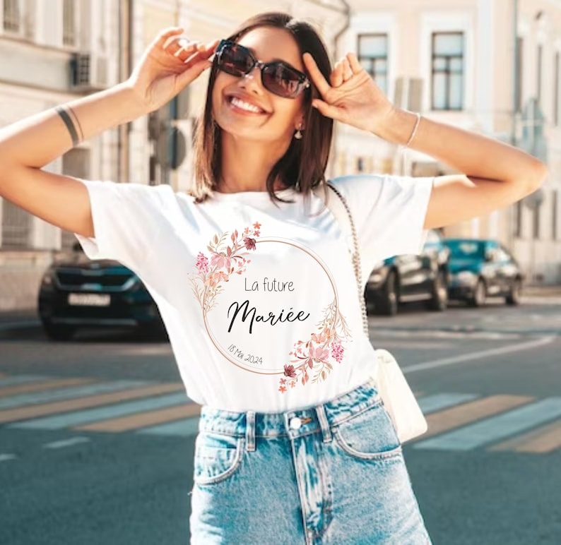 May include: White t-shirt with a floral wreath design and the text "La future Mari&eacute;e" in black script. The design includes pink and peach-colored flowers and the date "18 Mai 2024".