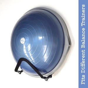 Puede incluir: Un entrenador de equilibrio BOSU Pro azul con un soporte de pared negro. El entrenador de equilibrio está montado en una pared blanca.