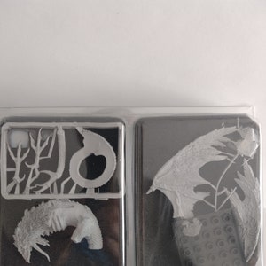 May include: A white plastic model kit of a dragon with wings, tail, and head pieces. The model is packaged in a clear plastic tray with a black foam backing.