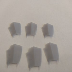 Op de afbeelding: Zes grijze plastic schilden met een puntige onderkant. De schilden zijn gerangschikt in twee rijen van drie.