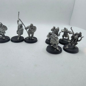 May include: A set of nine unpainted metal miniatures depicting orcs. The miniatures are posed in various fighting stances, some holding swords, spears, and bows. The miniatures are on black bases.