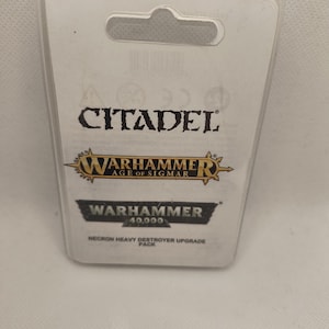 Può includere: Una confezione blister in plastica bianca con un'etichetta nera e dorata. L'etichetta riporta "Citadel", "Warhammer Age of Sigmar" e "Warhammer 40.000 Necron Heavy Destroyer Upgrade Pack".