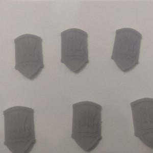 Puede incluir: Seis escudos de plástico gris con un diseño en relieve de una vela de barco y un mástil.