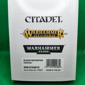 May include: A white box with a black and white image of a Warhammer 40,000 logo. The box is labeled "Eldar Swooping Hawks" and has a barcode and the text "Made in the UK".