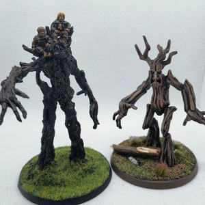 May include: Two painted miniature figures of tree-like creatures. The figure on the left is larger and has two smaller figures perched on its head. The figure on the right is smaller and has a more humanoid shape. Both figures are painted in shades of brown and have a rough, bark-like texture.