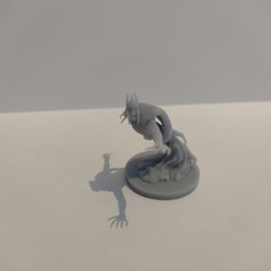 Op de afbeelding: Een grijs 3D-geprint miniatuur van een spookachtige figuur met hoorns en een vloeiende cape. De figuur is geposeerd in een dramatische, zwaaiende pose, met zijn armen uitgestrekt. Het miniatuur staat op een ronde basis.