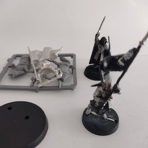 May include: Two unpainted miniature figures, one on a black base and one on a gray base, with a gray plastic sprue containing a miniature figure on a horse.