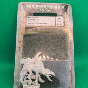 May include: A Warhammer 40,000 Kroot Hounds miniature figure in a plastic package. The figure is a detailed, silver-colored creature with a dynamic pose. The packaging includes text in multiple languages, including English and Spanish.