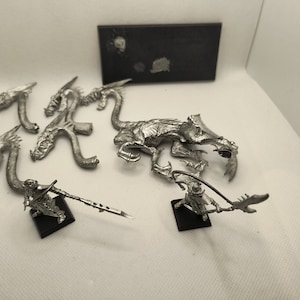 May include: A set of miniature metal figures for a tabletop game. The set includes a dragon with multiple heads, a warrior with a spear, and a base for the figures.