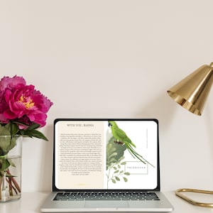 Może przedstawiać: Laptop wyświetla stronę książki z tekstem "WITH YOU, RADHA" i "VRINDAVAN". Strona zawiera akwarelową ilustrację zielonej papugi i liści. Bukiet różowych piwonii w szklanym wazonie i złota lampa biurkowa są również widoczne.