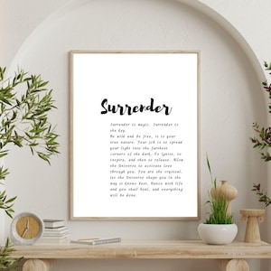 May include: A framed print with the word "Surrender" in a stylish script font. The print includes a poem about surrender and is displayed on a wooden shelf with decorative items and greenery.