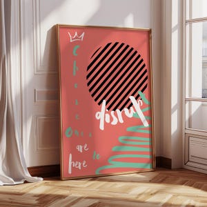 May include: Framed art print with a coral background, featuring a black and white striped circle and the word "disrupt" in white. Additional text includes "choose ones are here to" in white and teal. A gold frame surrounds the artwork.
