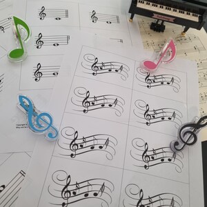 Può includere: Un set di flashcard di note musicali con illustrazioni in bianco e nero di note musicali su una chiave di violino. Le flashcard sono stampate su carta bianca e hanno un avviso di copyright in fondo. Ci sono anche diversi clip di note musicali in plastica colorata.