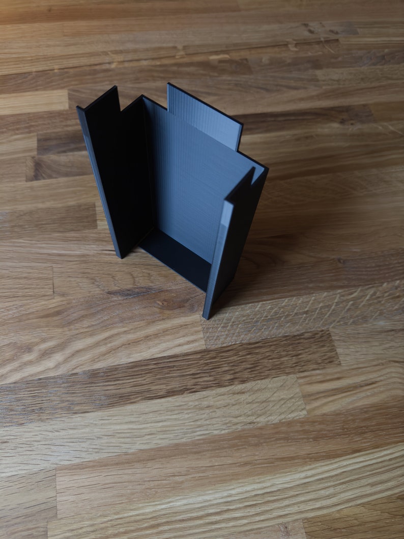 May include: A black plastic box with a rectangular opening. The box is made of a textured material and has a smooth, flat surface.