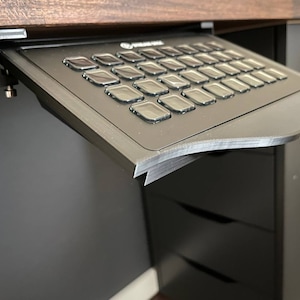 以下が含まれることがあります： 黒い、机の下のキーボードトレイ。曲線的なエッジとフルサイズのキーボードを備えています。トレイは木製の机の下に取り付けられており、部分的に拡張されています。キーボードは、複数のキーを備えた標準的なレイアウトです。