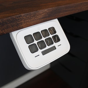 Pode incluir: Teclado branco com 10 botões e uma pequena tela. O teclado está montado sob uma superfície de madeira.