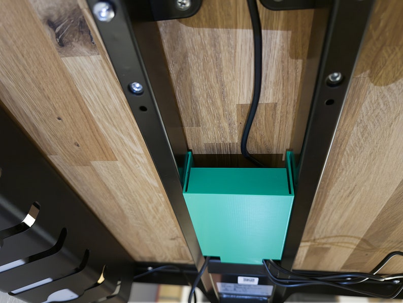 May include: Underside of a wooden desk with a black metal frame and a green plastic cable management box.