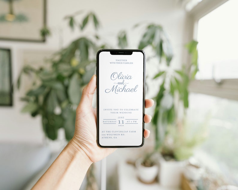 May include: A smartphone displaying a wedding invitation for Olivia and Michael. The invitation is for a wedding on Saturday, June 11th, 2023 at 5 PM at the Cloverleaf Farm in Athens, GA.