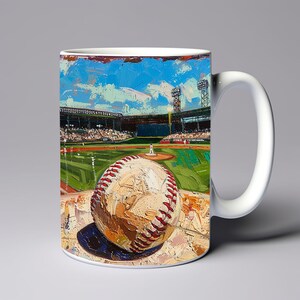May include: White ceramic mug with a colorful painting of a baseball on a green field. The painting depicts a baseball stadium with a blue sky and white clouds. The baseball is in the foreground and is in focus.