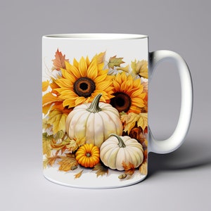 May include: White ceramic mug with a fall-themed design featuring sunflowers, pumpkins, and autumn leaves. The sunflowers are yellow with brown centers, and the pumpkins are white with a hint of yellow. The leaves are orange, yellow, and brown.