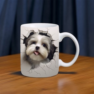 Op de afbeelding: Witte keramische mok met een 3D-afbeelding van een kleine, witte hond met grijs haar die uit een gebarsten muur kijkt. De hond heeft een roze tong die uitsteekt en kijkt recht naar de kijker.