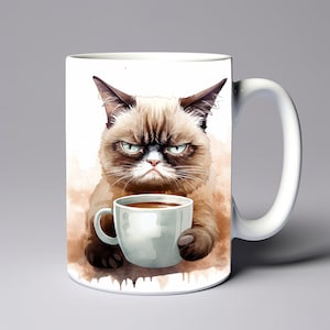 May include: White ceramic coffee mug featuring a watercolor illustration of a grumpy cat holding a coffee cup. The cat has a brown and tan coat with green eyes and a perpetually annoyed expression. The mug has a white handle.