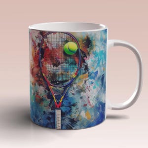 May include: White ceramic mug featuring a colorful artistic design of a tennis racket and ball. The artwork includes a tennis racket with a yellow tennis ball, set against a backdrop of vibrant paint splatters in various colors.