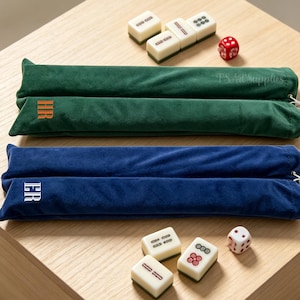 May include: Two long, rectangular velvet pouches in dark green and navy blue, each featuring a white drawstring closure. The green pouch is embroidered with orange initials HR, and the blue pouch with white initials ER. Mahjong tiles and dice.