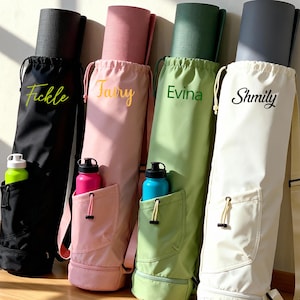 May include: Four yoga mat bags in black, pink, green, and off-white, each with a rolled-up yoga mat inside. Each bag has a pocket holding a water bottle. The bags are personalized with names in script: Fickle, Tary, Evina, and Shmily.