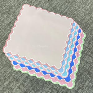 May include: A stack of pastel-colored, scalloped-edge placemats. The placemats are in shades of pink, blue, and green, with white and pink scalloped borders. The text "TS Art Supplies" is visible in the background.